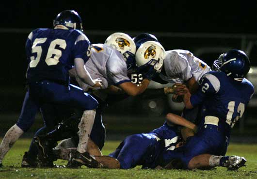 Ian Shuttleworth (12), Daniel Richards (18), Tim Kelly (52) and Hayden Stewart (56) swamp Sheridan quarterback Dylan Flores. (Photo by Rick Nation)