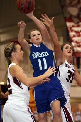 Logan Davis (11) goes to the off-hand on a shot between Benton's Bailey Gately, left, and Madi Brooks (35). (Photo by Rick Nation)