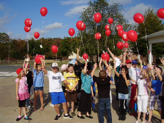 Third grade students release red balloons.