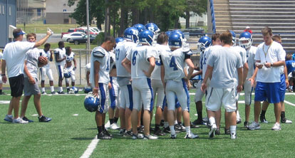 New Bryant offensive coordinator Lance Parker, right, checks on his playlist before calling a play for the offense while head coach Paul Calley, left, gives some individual instruction.