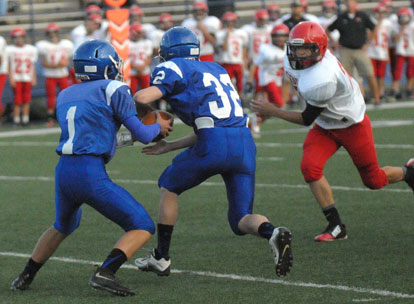 Running back Dalen McDonald (32) and quarterback Jake Meaders work the read option as a Cabot Red defender bears down. (Photo by Kevin Nagle)