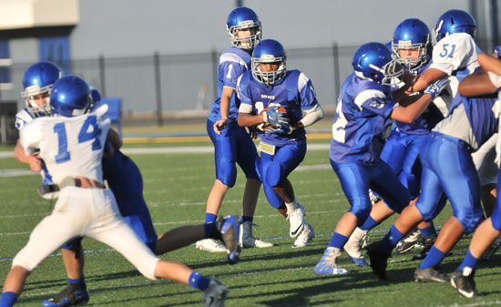 Bryant Blue running back Xavier Foote takes a handoff from quarterback Garrett Wilson as players tangle at the line of scrimmage. (Photo by Kevin Nagle)